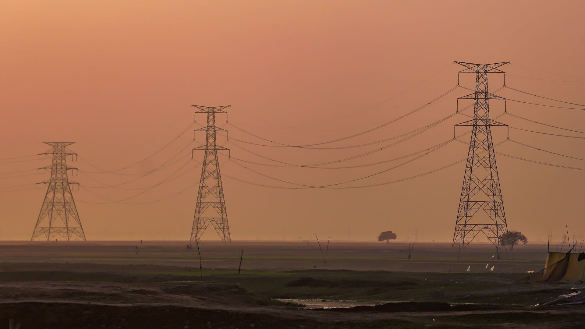 Transmission towers silhouetted against a golden sunset over open plains